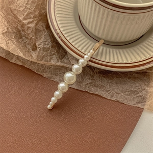 Close-up of elegant gold metal hair clip featuring a row of gradient white faux pearls