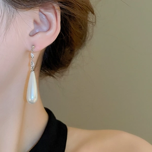 Detailed view of teardrop pearl drop earrings with sparkling crystal accents on model