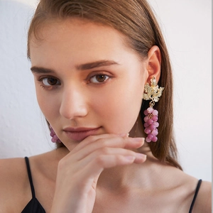 Realistic purple grape earrings with gold leaves worn by a model in a side profile view