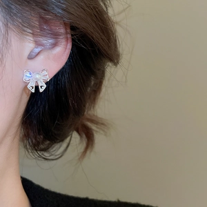 Detail of bow-shaped earring with pearl and zircon inlay worn on a female model