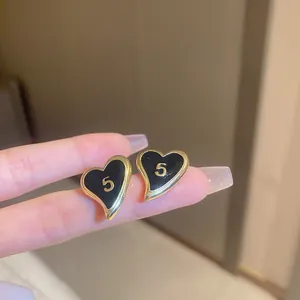Macro detail of heart-shaped black enamel earrings with golden number 5 and metal trim