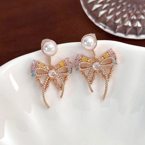 Macro shot of elegant zircon bow earrings with pearls hanging on a white ceramic bowl