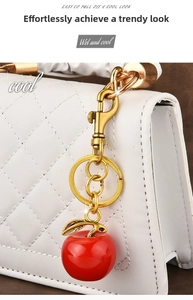 Macro view of a glossy red apple keychain with golden leaf on white quilted bag