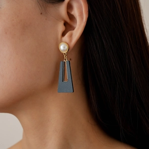 Detail of square gold hoop earring with white pearl and matte black geometric pendant