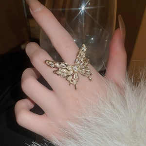 Detail of gold butterfly ring with pearls and zircons worn by model holding a glass