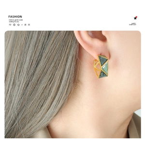 Close-up of geometric gold-plated earrings with green enamel on model ear