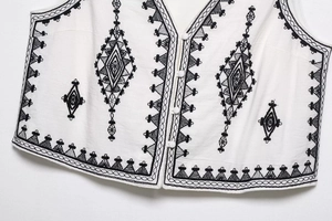 Detailed close-up of geometric black embroidery and white buttons on ethnic vest