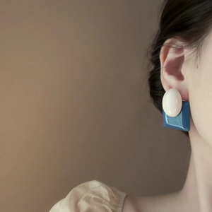 Close-up of geometric white and blue resin earrings on a model with soft lighting