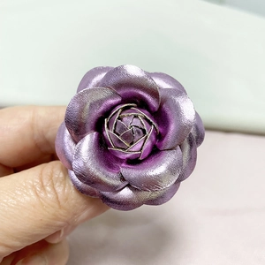 Detail of premium purple metallic camellia flower brooch with leather-like texture finish