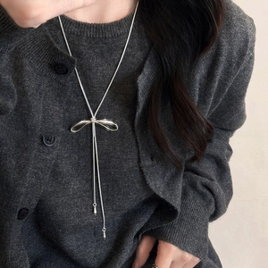 Detail of silver bow adjustable necklace worn on grey knitwear for a minimalist look
