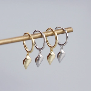 Elegant gold and silver conch shell hoop earrings hanging on a metal rod for display