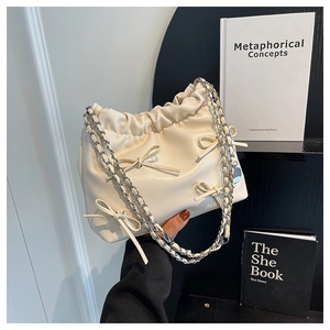 Detail of cream leather tote featuring ribbon bows and silver chain strap held by model