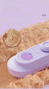 Detail of the self-cleaning button on a purple pet massage brush for deshedding