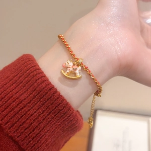 Gros plan du pendentif cheval à bascule plaqué or 24K sur un bracelet tressé rouge
