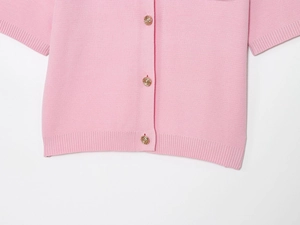 Dettaglio del top in maglia rosa con bottoni dorati a rilievo e texture a costine