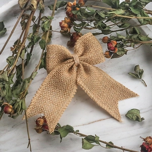 Rustic burlap swallowtail bow made of natural jute on marble plate with dried roses