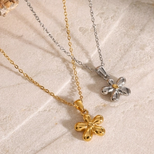 Polished gold and silver stainless steel flower pendant necklaces on stone surface