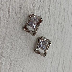 Detail of silver lava earrings with rectangular zircon stones on textured background