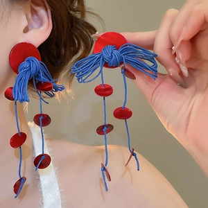 Detail of red circular shell stud earrings with blue wax rope tassels on female model