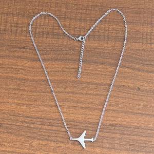 Vue détaillée du pendentif avion argenté avec fermoir mousqueton sur fond en bois