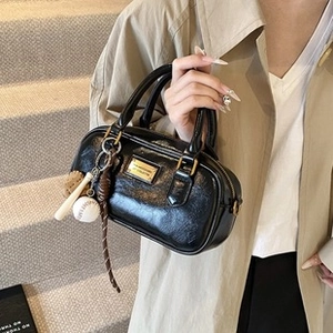 Close-up of black glossy Boston bag with unique mini baseball and bat keychain charms