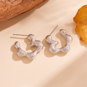 Detailed close-up of silver C-shape stud earrings with irregular bubble texture on leather