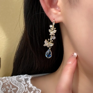 Detail of butterfly zircon earrings with a blue teardrop stone on a model's ear