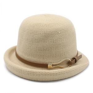 Detail of beige knit bucket hat featuring a brown leather strap and gold metal buckle
