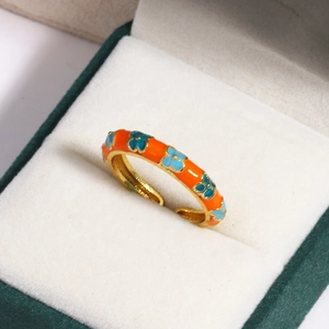 Close-up of orange enamel floral ring with blue flower pattern in a green velvet box