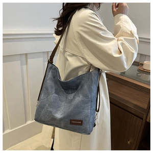 Detail of navy canvas tote bag featuring brown leather logo and adjustable shoulder strap