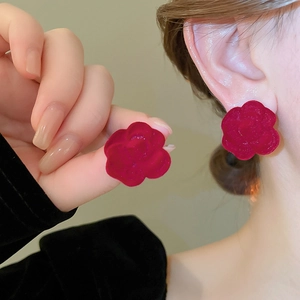 Detailed view of elegant red velvet rose stud earrings worn on a model's earlobe