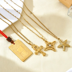 Assorted 18k gold plated stainless steel pendants with star fish and cross on beige fabric