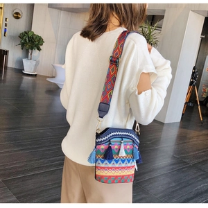 Ethnic woven bucket bag with blue tassels and geometric strap shown on model back