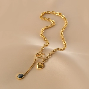 Gold chain necklace with heart pendant and oval gemstone on beige silk fabric