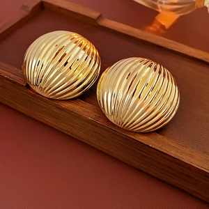 Detailed view of golden round earrings with textured striped surface on a wooden tray