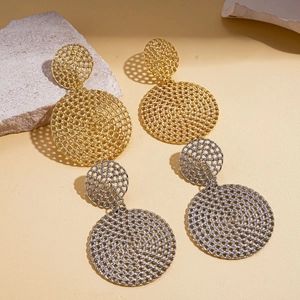 Gros plan de boucles d'oreilles en maille géométrique dorées et argentées sur pierre beige