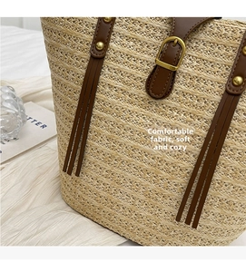 Close-up of woven straw tote bag with brown leather strap and gold metal buckle detail