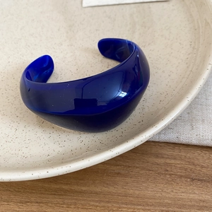 Detailed close-up of dark blue chunky acrylic open bangle on a ceramic display plate