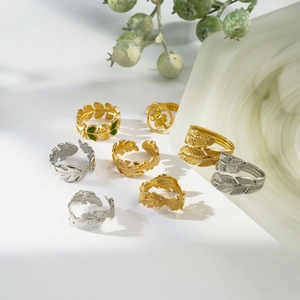 Artistic layout of gold and silver steel leaf, feather, and clover rings on white surface
