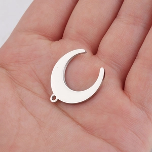Macro view of a mirror-polished stainless steel crescent moon pendant held in a palm