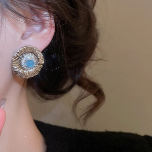 Close-up of vintage sunflower stud earring with blue stone and sparkling zircon halo
