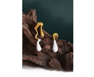 Macro shot of asymmetric gold-plated earrings with white enamel water drops on wood