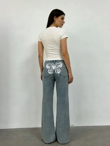 Dettaglio dei jeans azzurri che mostra la stampa a farfalla bianca sulla tasca posteriore