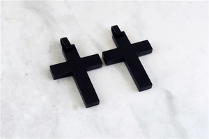 Detail view of two minimalist black matte stainless steel cross pendants on marble background