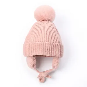 Detail view of pink knit baby beanie with faux fur pom pom and earflaps for winter