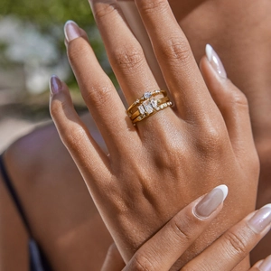 Detail of three stacked gold steel rings with round and emerald cut zircon stones