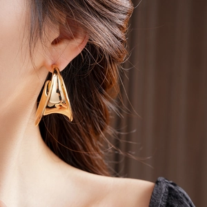 Close-up of model wearing thick gold wide C-shaped earrings in deconstructed style