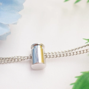 Minimalist silver cylindrical pendant with a fine cable chain on a textured background