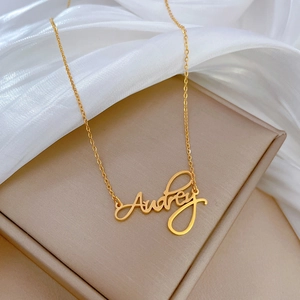 Detailed view of golden Audrey name necklace on a premium beige jewelry display stand