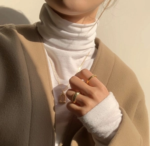 Close-up of minimalist gold U-shape necklace and polished rings on a female model